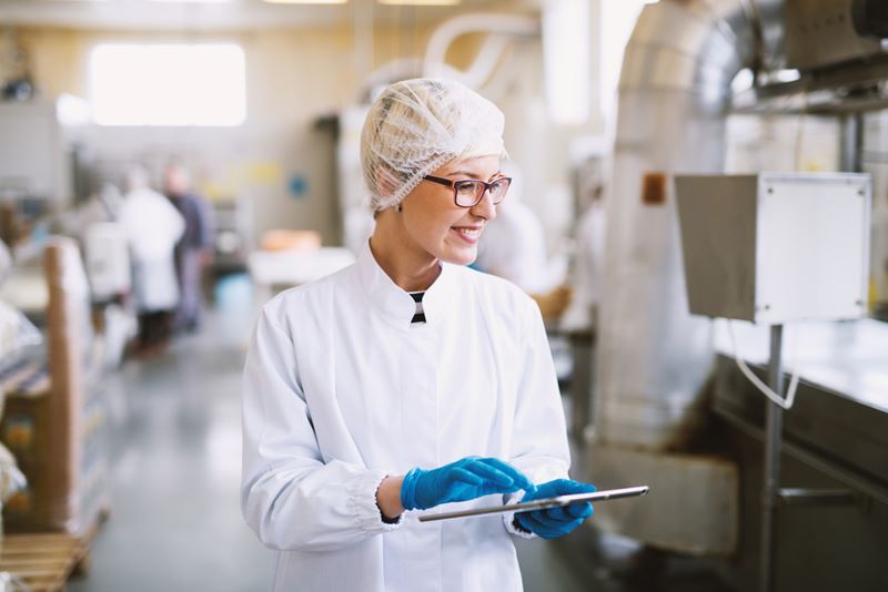 A woman in a factory is wearing glasses, blue gloves and a hair net